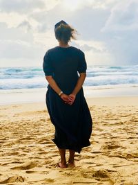 Rear view of woman standing at beach against sky