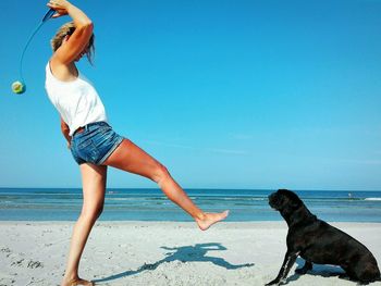 Woman playing fetch with black dog on beach