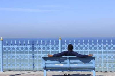 Rear view of man sitting on railing against sea