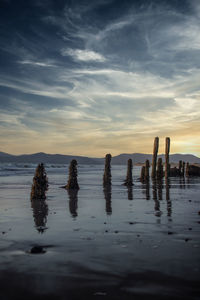 Wooden posts in sea against sky during sunset