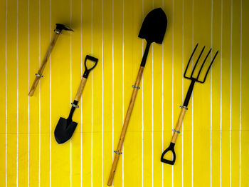 Close-up of gardening equipment on yellow wall