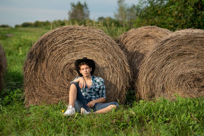 Portrait of young man sitting on field near the haystack 