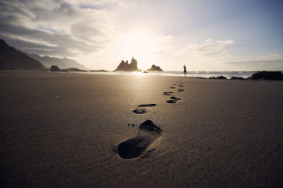 Footprints in sand against silhouette of person. man walking along beach to sea at golden sunset.