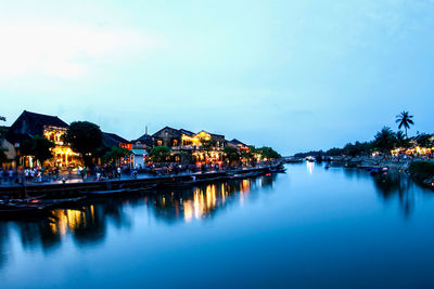 Illuminated buildings by lake against sky at dusk