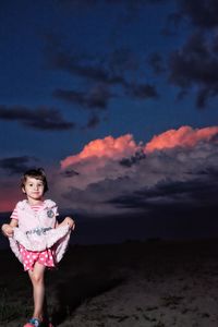 Portrait of girl standing on field against cloudy sky at dusk