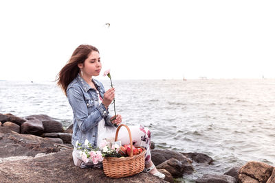 Young woman sitting on wicker basket on land against sky