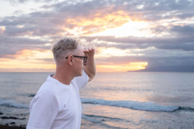 Side view of woman looking at sea against sky during sunset