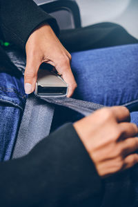 Closeup image of young woman fastens buckle on safety seat belt at airplane. travel concept