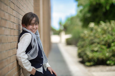 Child poses for fashion leaning on corner, sympathetic and laughing. boy with straight brown hair.