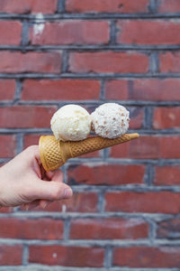 Close-up of hand holding ice cream cone against brick wall