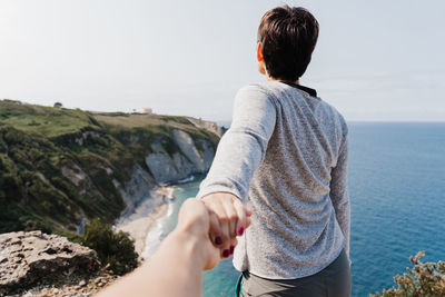 Lesbian couple holding hands while standing by sea against sky