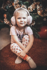 Portrait of cute girl sitting by christmas tree