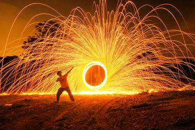 Men standing by spinning wire wool on field at night