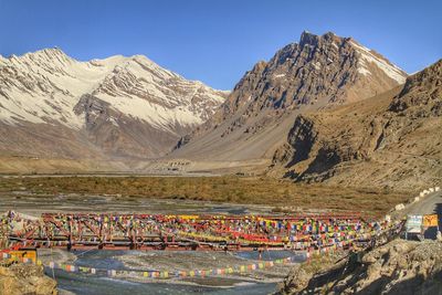 Bridge with prayer flags over river against mountains and sky