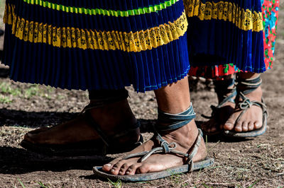 Low section of women wearing traditional clothing and footwear standing on field during sunny day