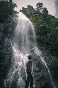 Rear view of man standing against waterfall