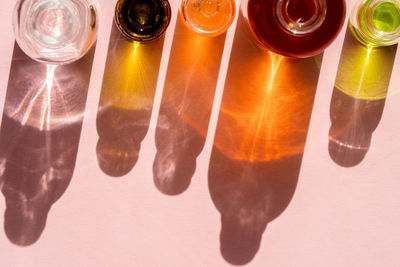 Different cosmetic glass bottles on pink background. pattern by shadows and illuminating reflections