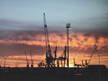 Silhouette cranes at commercial dock against sky during sunset