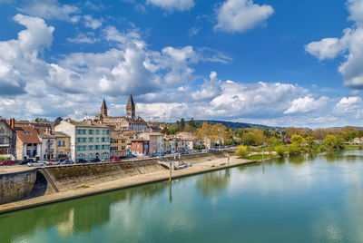 View of buildings by river against cloudy sky