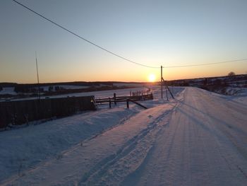 Snow covered land against clear sky during sunset