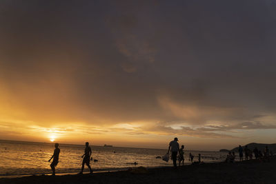 Silhouette people on beach against sky during sunset