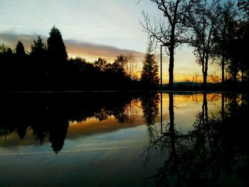 Reflection of silhouette trees in lake against sky at sunset