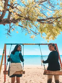 Portrait of women sitting on swing at beach against sky