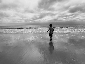 Rear view of woman walking at beach against sky