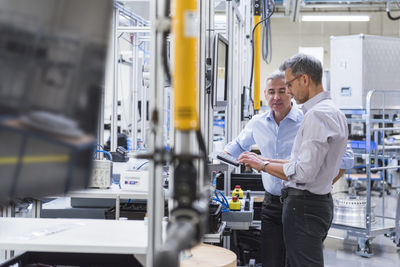 Two businessmen in modern factory hall using computer