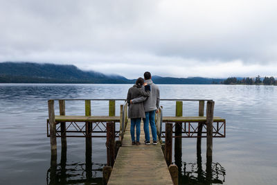 Rear view of couple standing on pier by lake against sky