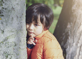 Portrait of cute boy against tree trunk