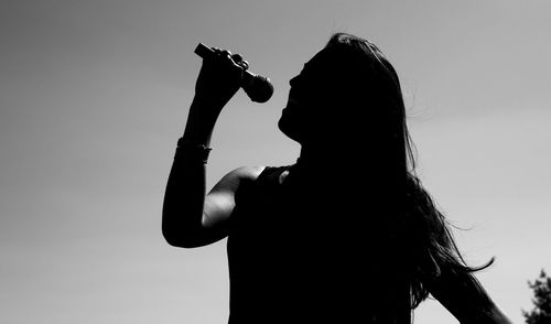 Silhouette woman singing on microphone against sky