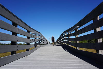 Man on footbridge against clear blue sky