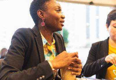 Content african american female with glass of beverage sitting at table with crop faceless female friend while spending time together in cafeteria