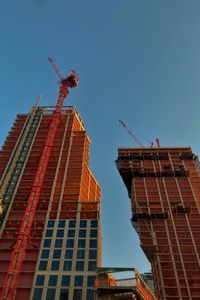 Low angle view of crane by building against clear blue sky