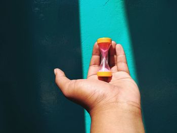 Close-up of hand holding bottle against blue wall