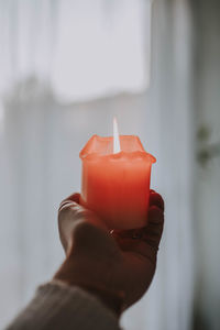 Cropped hand of woman holding candle against curtain