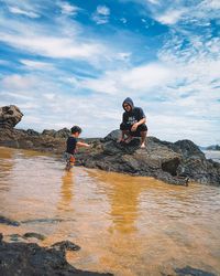 People on rock at beach against sky