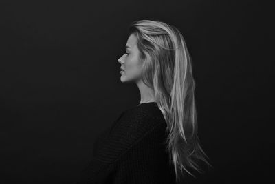 Side view of young woman standing against black background