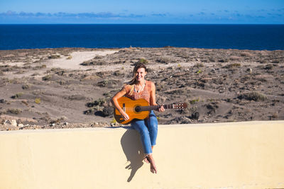 Full length of man sitting on guitar at beach