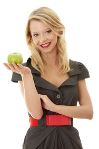 Portrait of smiling young woman holding apple against white background