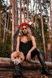 Portrait of young woman sitting on tree in forest