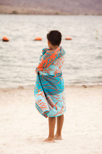 Boy wrapped in towel while standing at beach