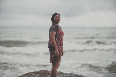 Young woman standing on beach against sky