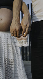 Midsection of man and pregnant woman holding baby booties while standing on floor