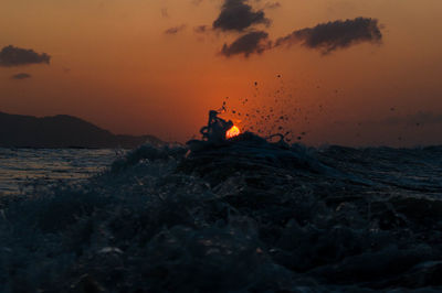 Silhouette rock on beach against sky during sunset