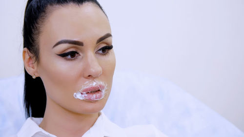 The patient sits in the cosmetology clinic with a superimposed anesthetic cream pad on the lips