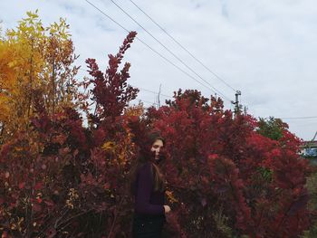 Portrait of young woman standing by plants against sky