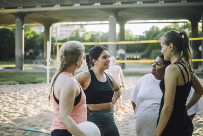 Multiracial female friends talking together while playing volleyball