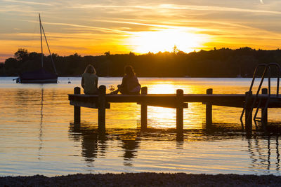 Rear view of female friends resting on jetty over lake during sunset